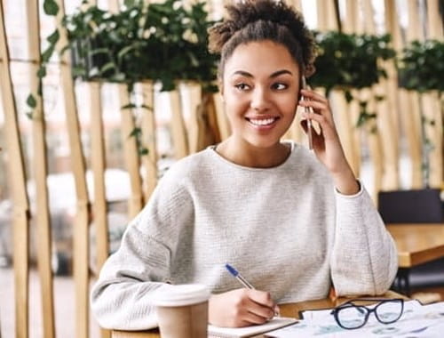 Woman at a table outdoors with pen in hand and a notebook