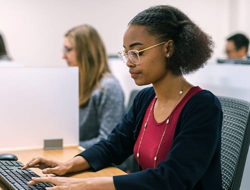 exam room young student black woman wearing glasses red top black cardigan sitting typing at a computer keyboard