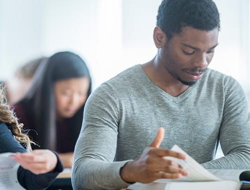 young students studying sitting in a classroom exams reading textbook turning page